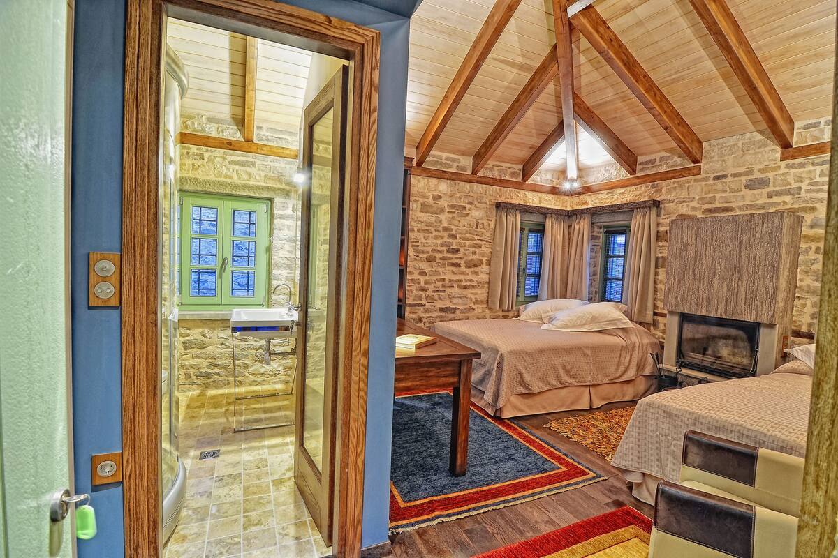 A cozy room with a stone wall, wooden beams, a bed, a table, and a fireplace.