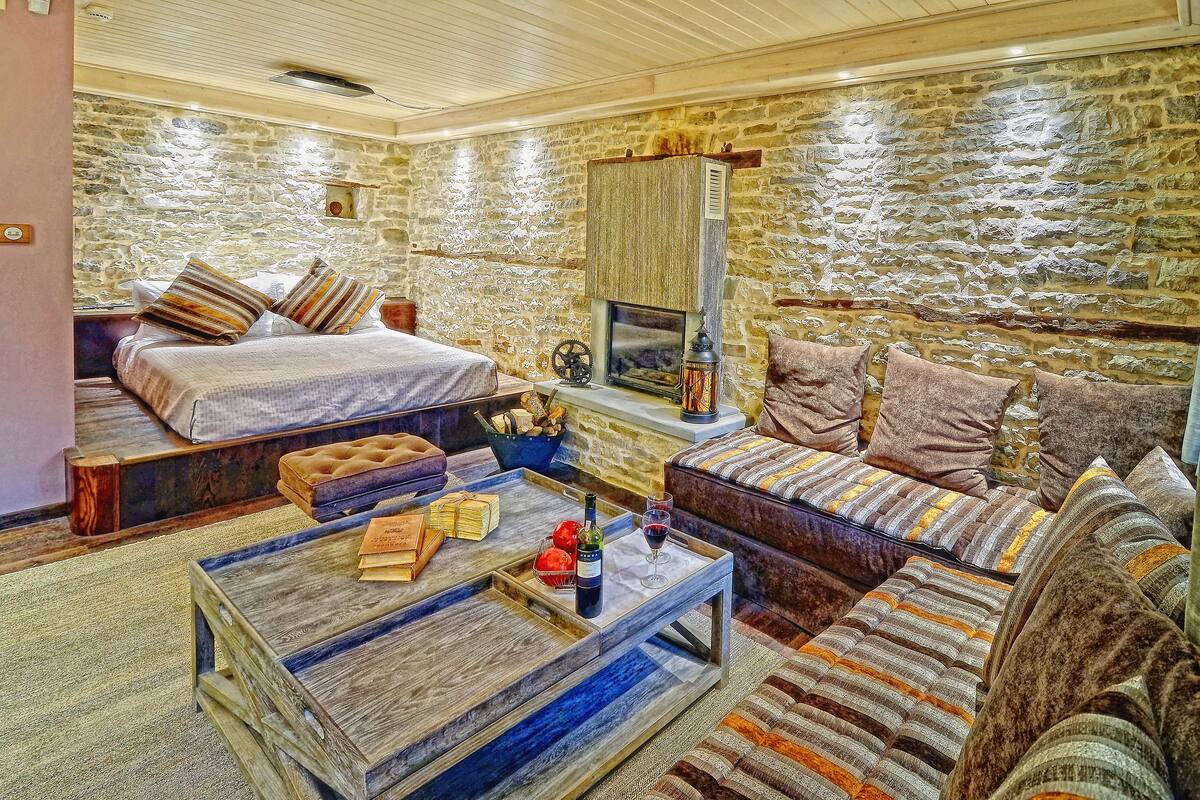 A cozy room with a stone wall, a bed, a sofa, a coffee table, and a fireplace.