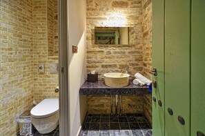 Un baño con pared de piedra, encimera de mármol, lavabo redondo y puerta verde.