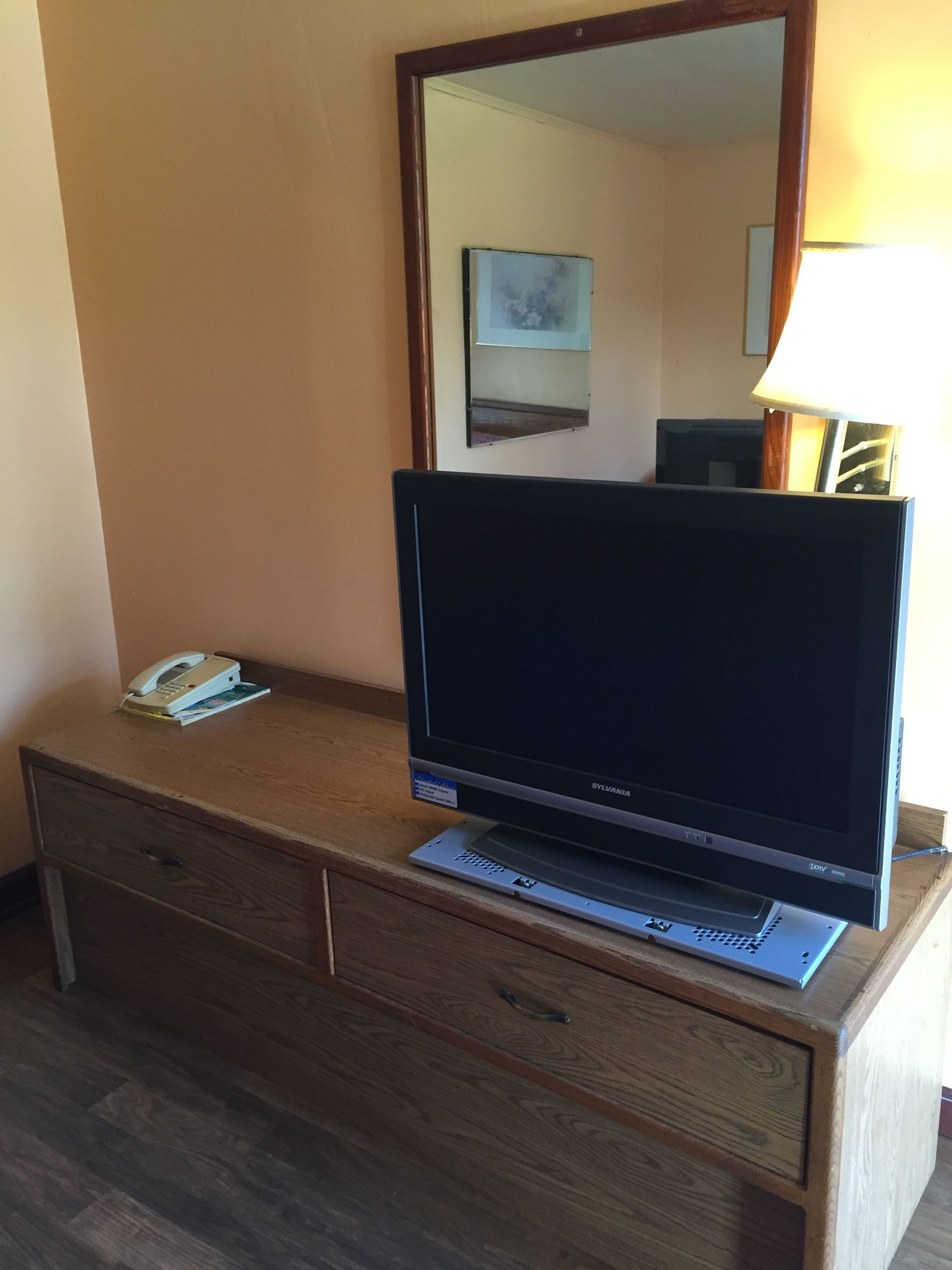 Habitación de hotel con escritorio de madera, televisor de pantalla plana, teléfono y lámpara.