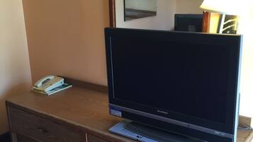Habitación de hotel con escritorio de madera, televisor de pantalla plana, teléfono y lámpara.