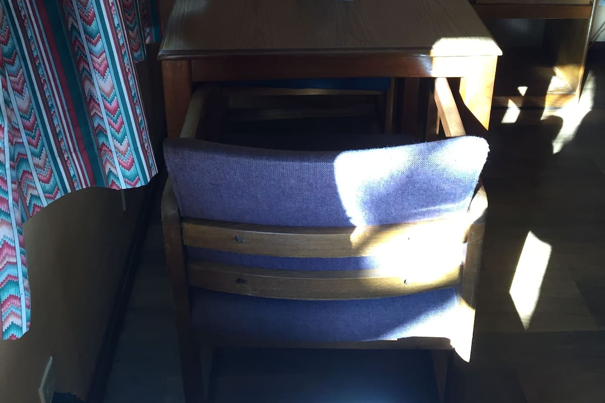 Quarto com mesa de madeira, uma cadeira, abajur e cortina estampada.