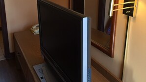 Une télévision posée sur une commode en bois, avec un miroir au-dessus et une lampe fixée au mur à côté de la télévision.
