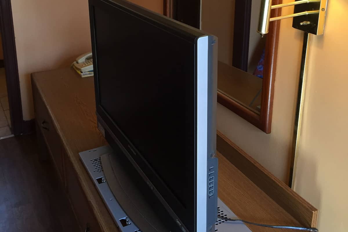 Uma televisão sobre um aparador de madeira, com um espelho acima e um candeeiro fixado na parede ao lado da TV.