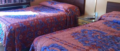 A hotel room with two beds, a nightstand, a lamp, and a framed picture on the wall.