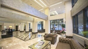 Un vestíbulo amplio con techo alto, una mesa de recepción, asientos cómodos y ventanas grandes.