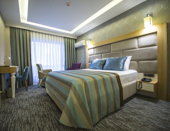 A hotel room with a large bed, a desk with a chair, a bedside table with a phone, and a window with curtains. - The Berussa Hotel (Bursa)
