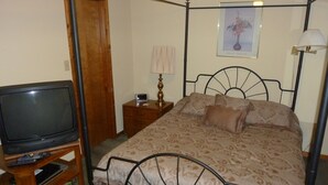 A bedroom with a four-poster bed, a television on a wooden stand, a bedside table with a lamp, and a framed picture on the wall. - Chapel Hill InnTown (Chapel Hill)