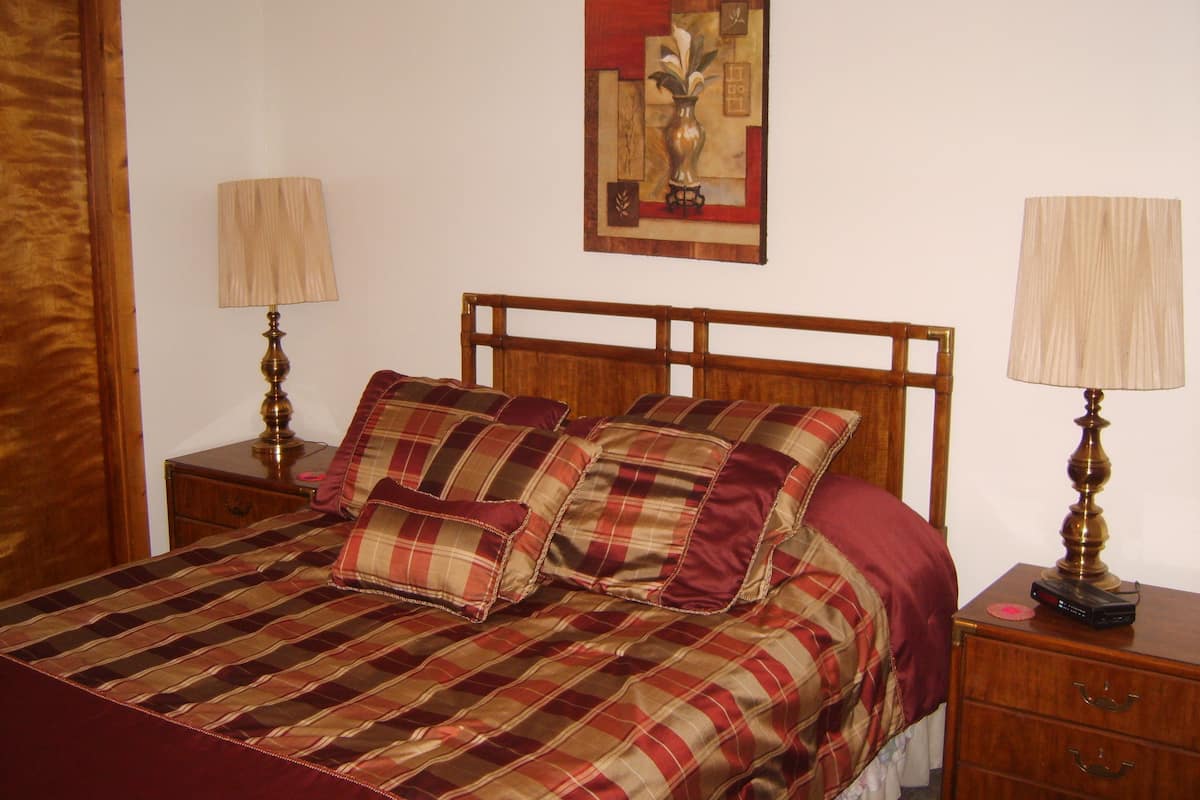 Un lit bien fait, avec une couette à carreaux, deux tables de chevet avec des lampes et une œuvre d’art encadrée accrochée au mur.
