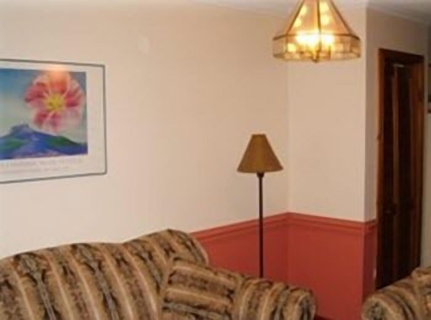 A room with a patterned sofa, a framed picture on the wall, a floor lamp, and a door.