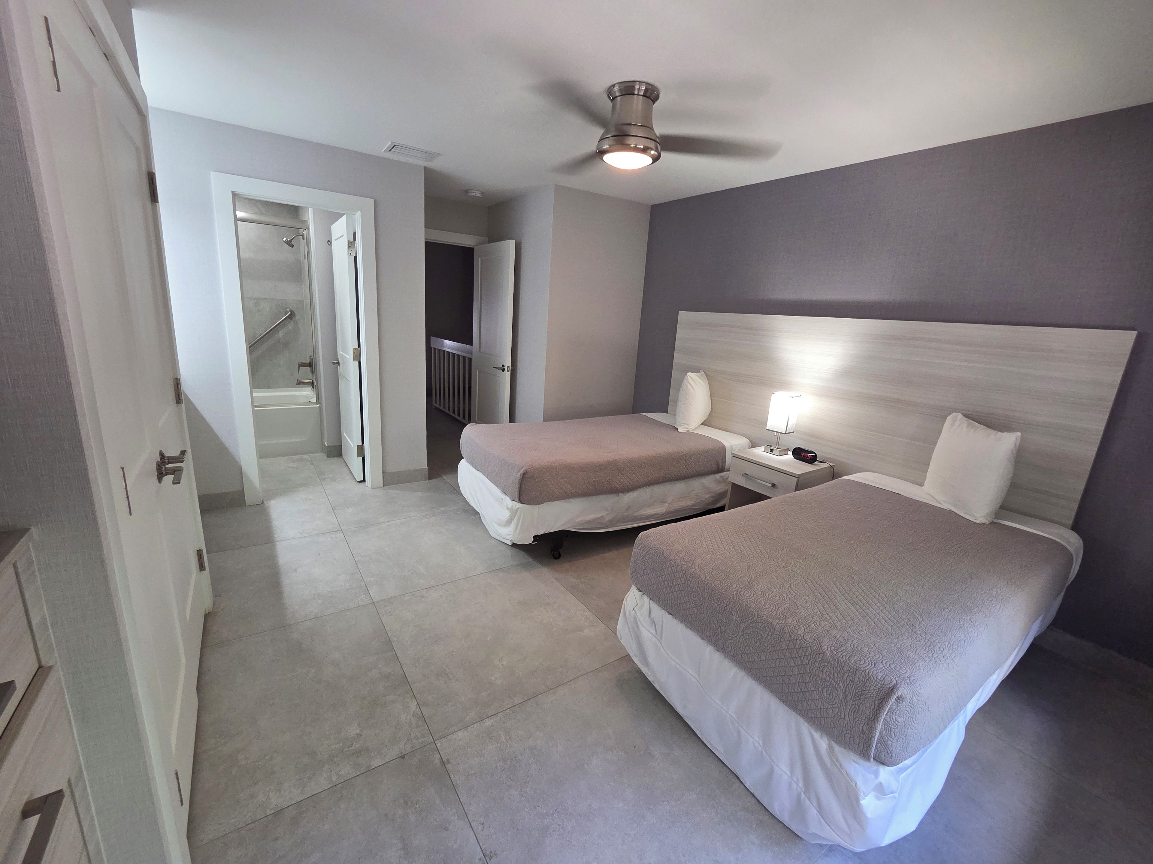 Een hotelkamer met twee bedden, een plafondventilator, een nachtkastje met lamp en een badkamer met douche en toilet.