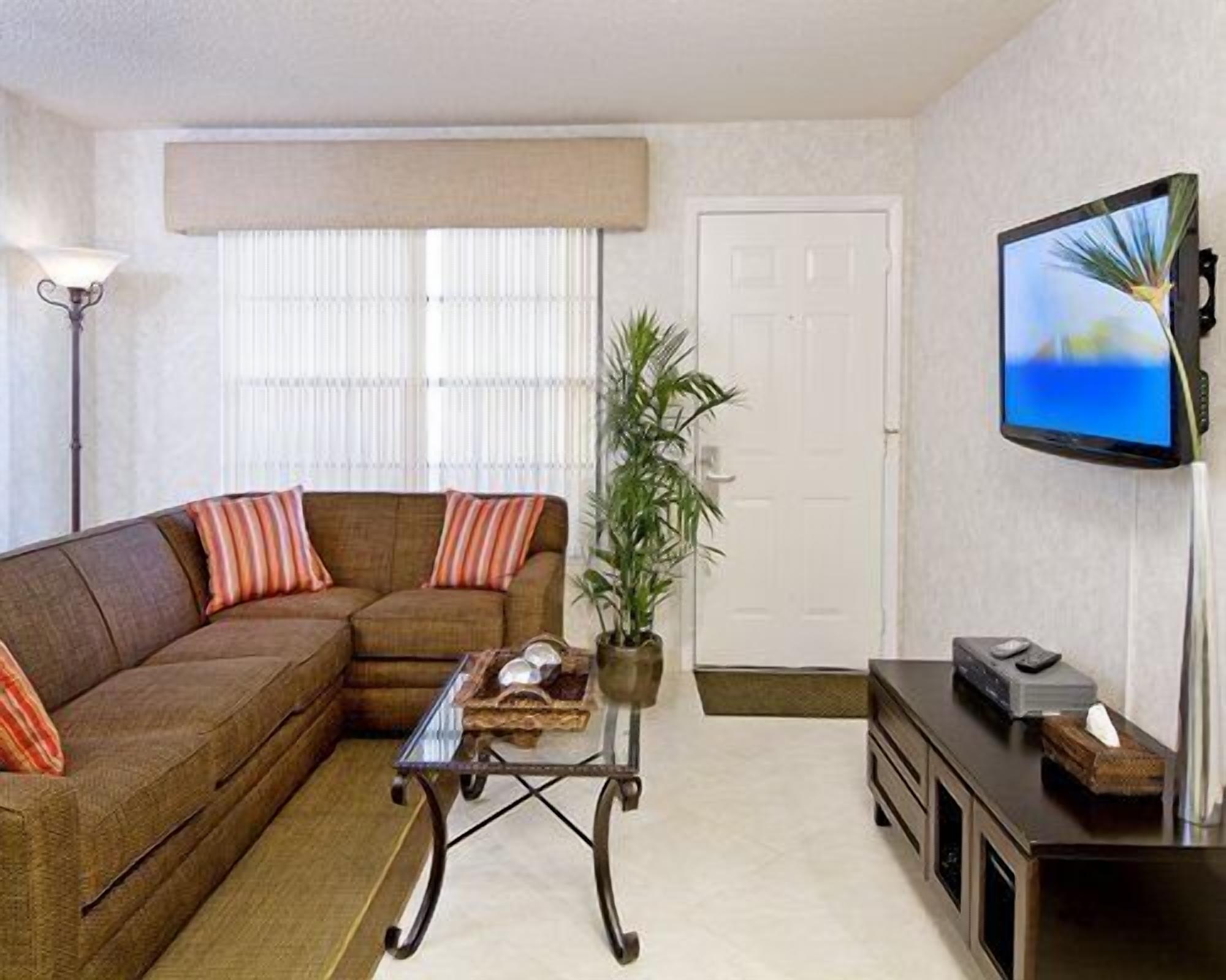 A living room with a sectional sofa, a coffee table, a television, and a potted plant.