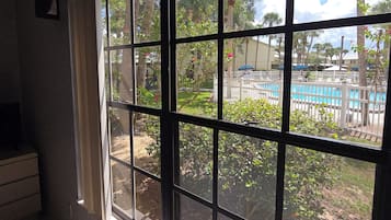 A room with a large window overlooking a pool area, a tiled floor, and a small piece of furniture on the left.