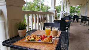 A breakfast table with waffles, strawberries, a croissant, and drinks on a covered patio with white railings and outdoor seating. - L'Oasis de l'Île, Refuge Urbain (Saint-Eustache)