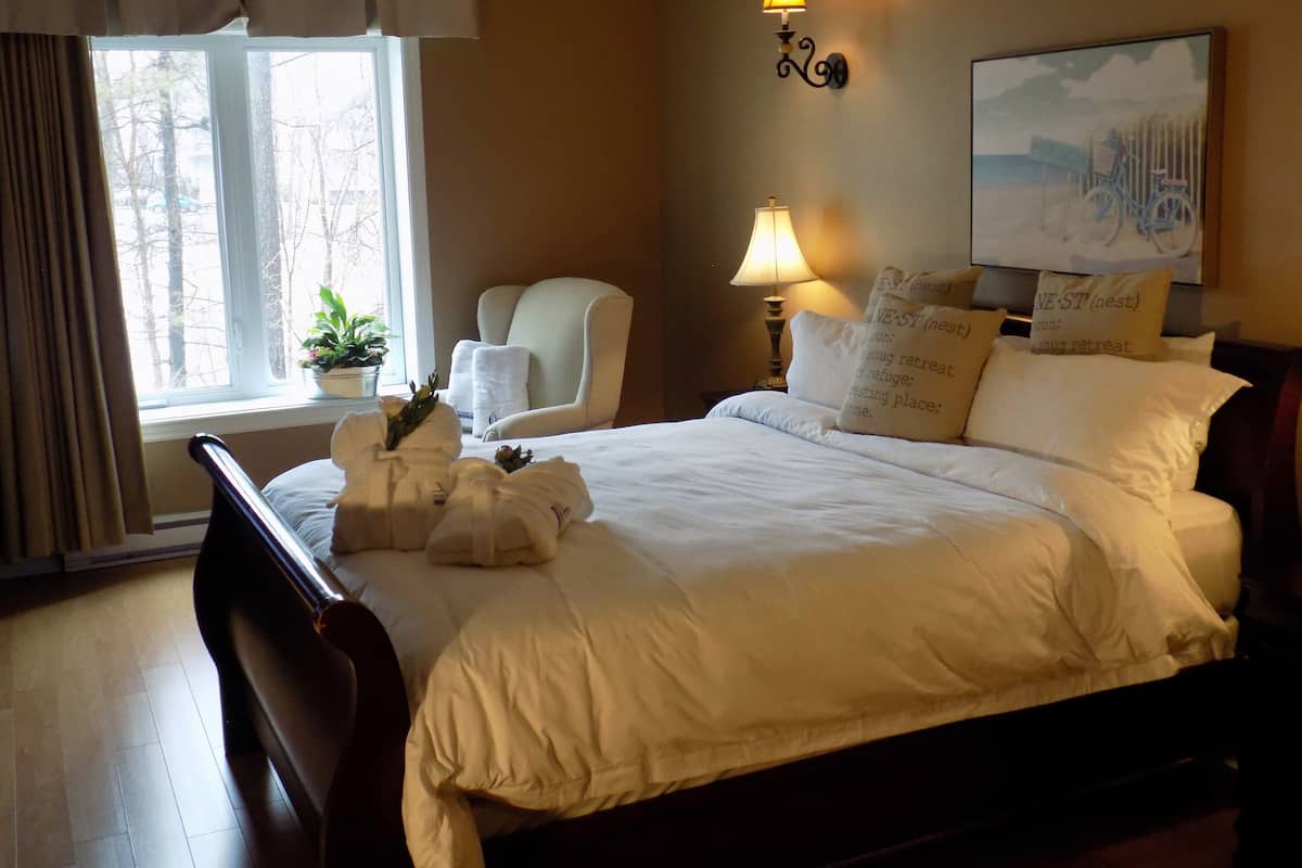 A neatly made bed with white linens, a bedside lamp, and a chair by the window.