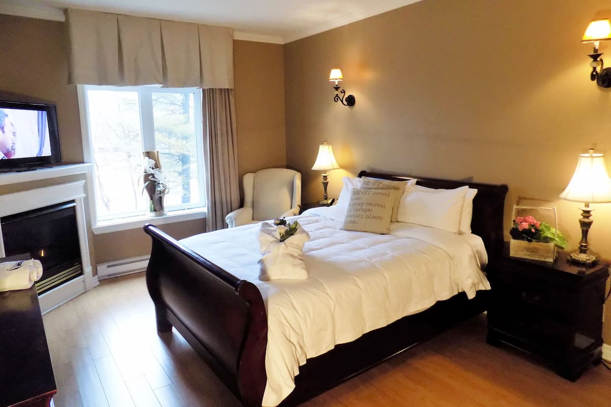 A hotel room with a large bed, a television, a chair, a fireplace, and two wall-mounted lamps.