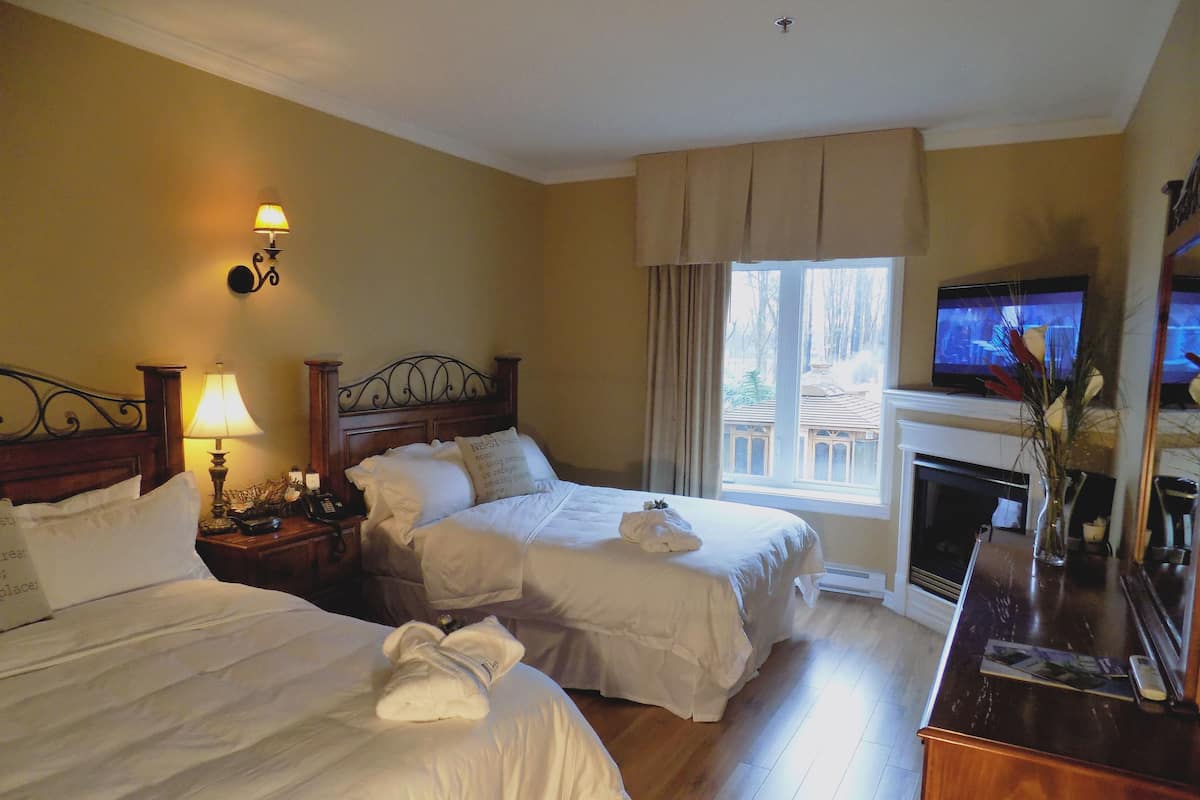 A hotel room with two beds, a television, a fireplace, and a window with curtains.