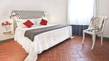 Una cama bien hecha con ropa blanca y almohadas rojas, una manta gris y un cabecero estampado.