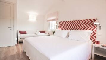 A bedroom with a large bed, a bedside table, a nightstand, a window with a view, and a door.