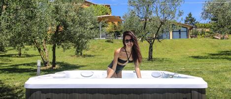A hot tub in a backyard with trees and a house in the background.