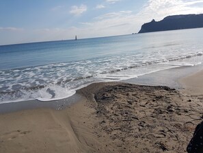 A beach with a rocky shoreline, waves gently lapping at the sand, and a distant lighthouse. - Da Agnese Locazioni brevi (Cagliari)