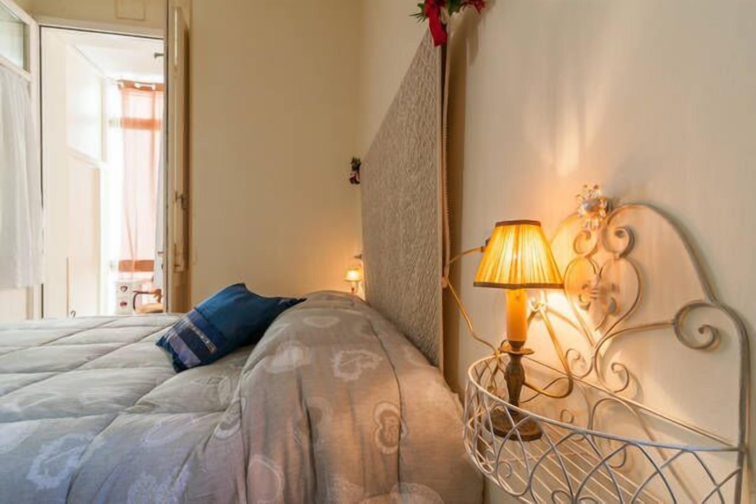Una cama bien hecha con una colcha estampada y una única almohada azul, una lámpara de pared y un adorno decorativo en la pared.