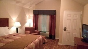 Una habitació d'hotel amb un llit, una cadira, un escriptori amb un ordinador, una finestra amb cortines i una porta.