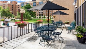 An outdoor patio with tables and chairs, a sign for Aspen Suites, and a building in the background. - Aspen Select (Rochester)