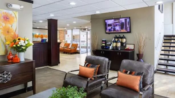 A lobby with leather chairs, a reception desk, a TV, and a coffee station. - Aspen Select (Rochester)