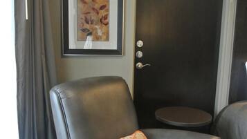 A single leather armchair with a floral pillow, a framed artwork on the wall, and a door with a round table beside it.