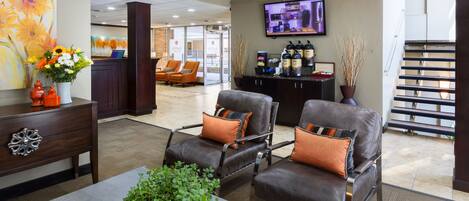 A lobby with leather armchairs, a reception desk, a TV screen, and a staircase.