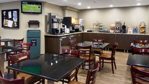 A restaurant with tables and chairs, a trash bin, a coffee machine, and a television displaying a sports game. - Aspen Select (Rochester)