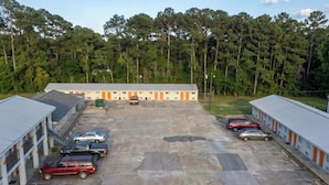 A motel with multiple rooms, a parking lot, and a forested background. - Budget Inn Jennings LA I-10 (Jennings)