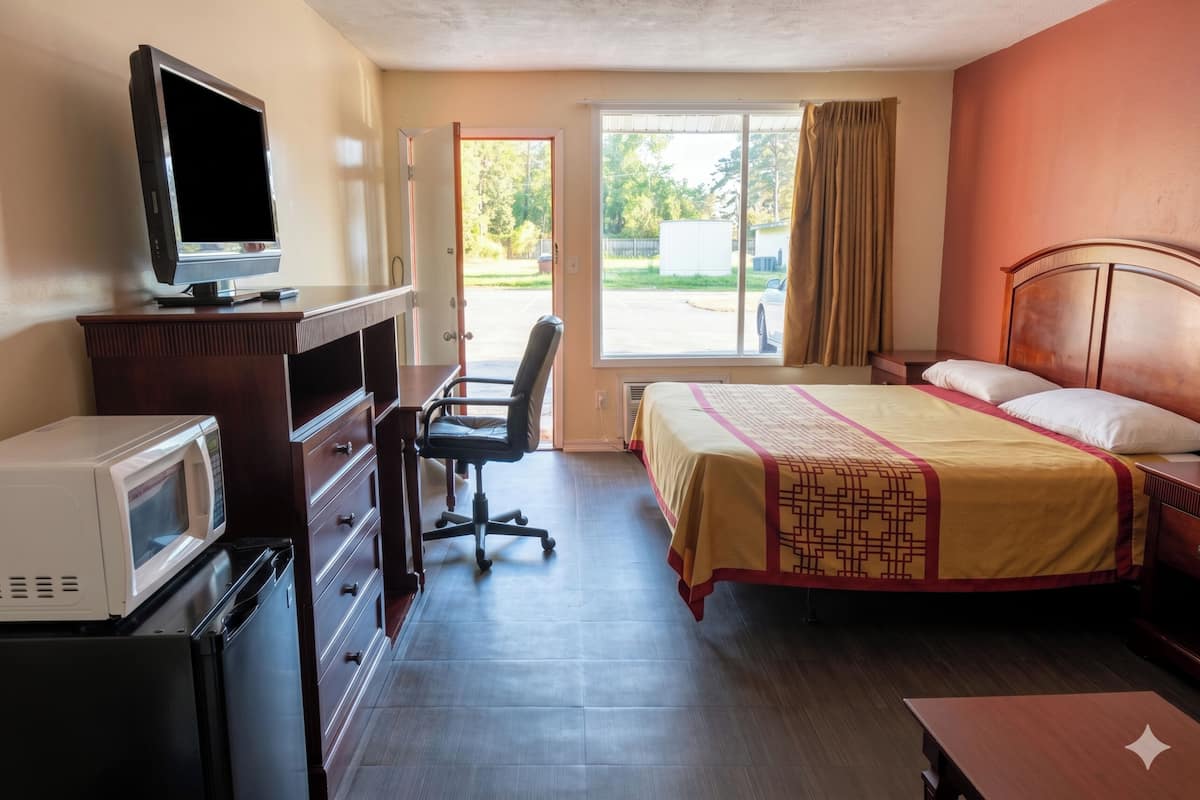 A hotel room with a bed, desk, chair, television, microwave, and a view of the outside.