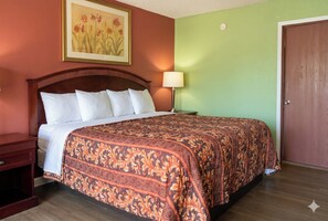 A hotel room with a bed, a nightstand, a lamp, a door, and a painting on the wall.