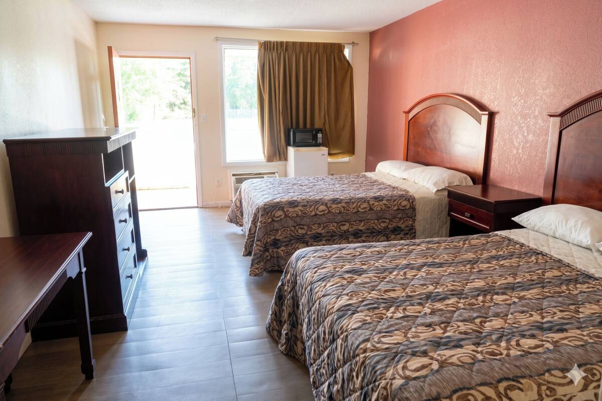 A hotel room with two beds, a desk, a dresser, a microwave, and a window with curtains.
