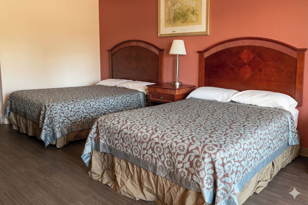 Two single beds with patterned bedding, a nightstand with a lamp, and a framed botanical print on the wall.