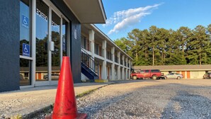 A building with a wheelchair-accessible entrance, a gravel parking area, and a red traffic cone. - Budget Inn Jennings LA I-10 (Jennings)