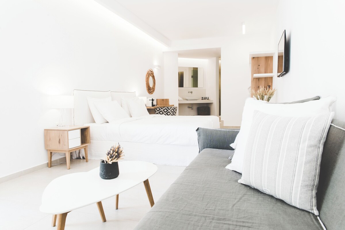 A modern, well-lit bedroom with a bed, bedside table, and a small desk with a mirror.