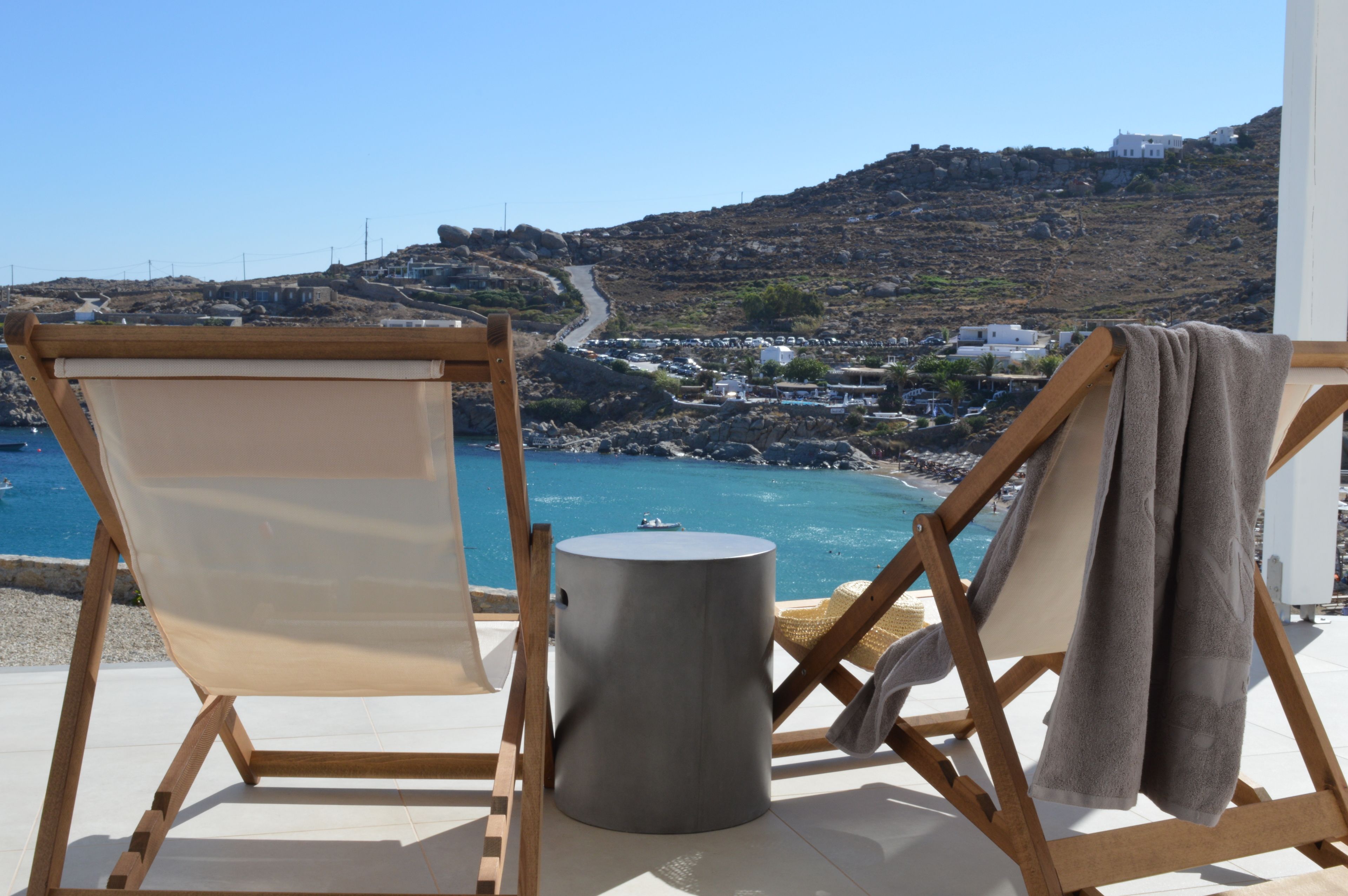 A seaside view with two wooden chairs and a small stool, overlooking a coastal town and a winding road.
