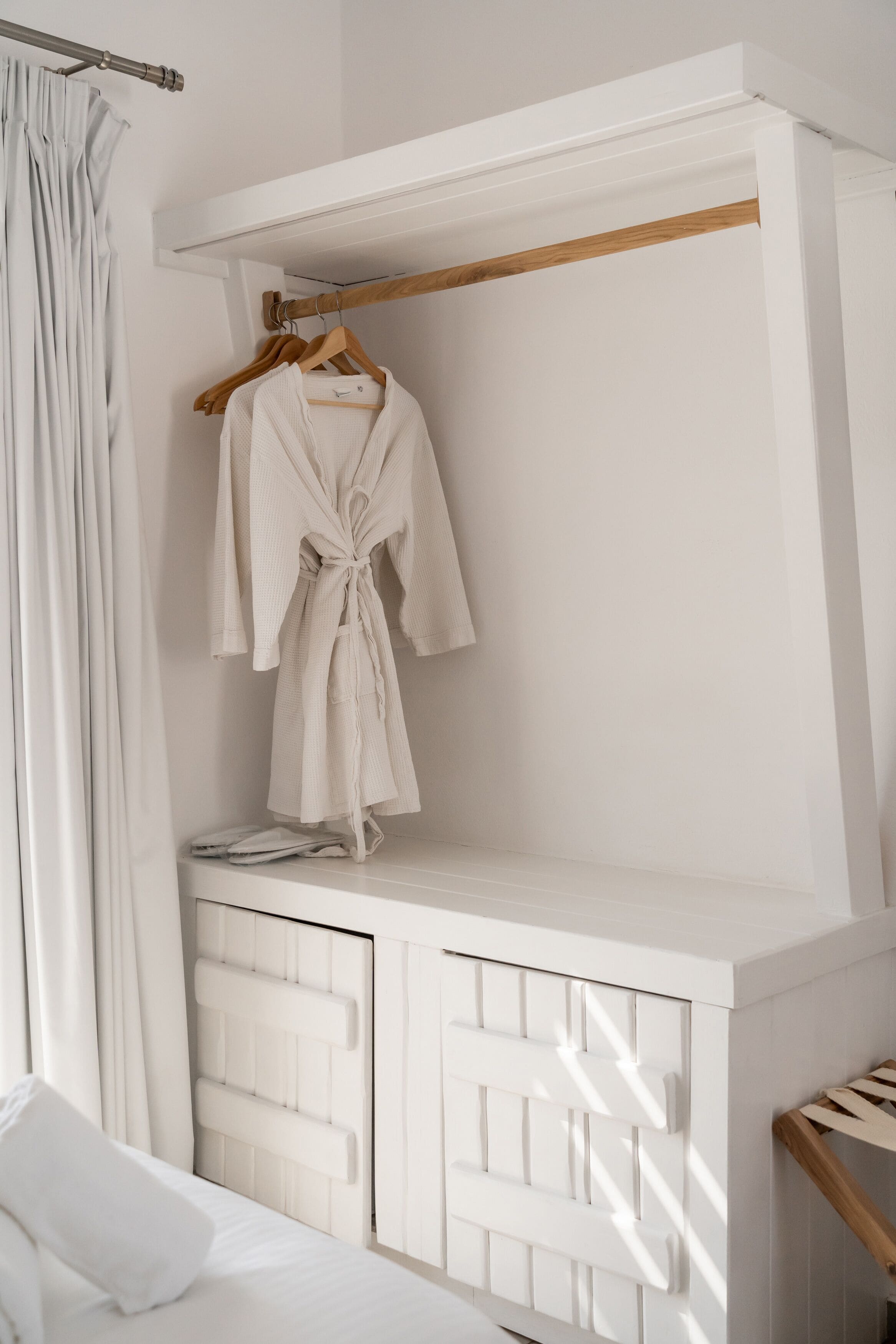 A white bathroom with a wooden shelf, a robe hanging on a wooden hanger, and a towel on the floor.