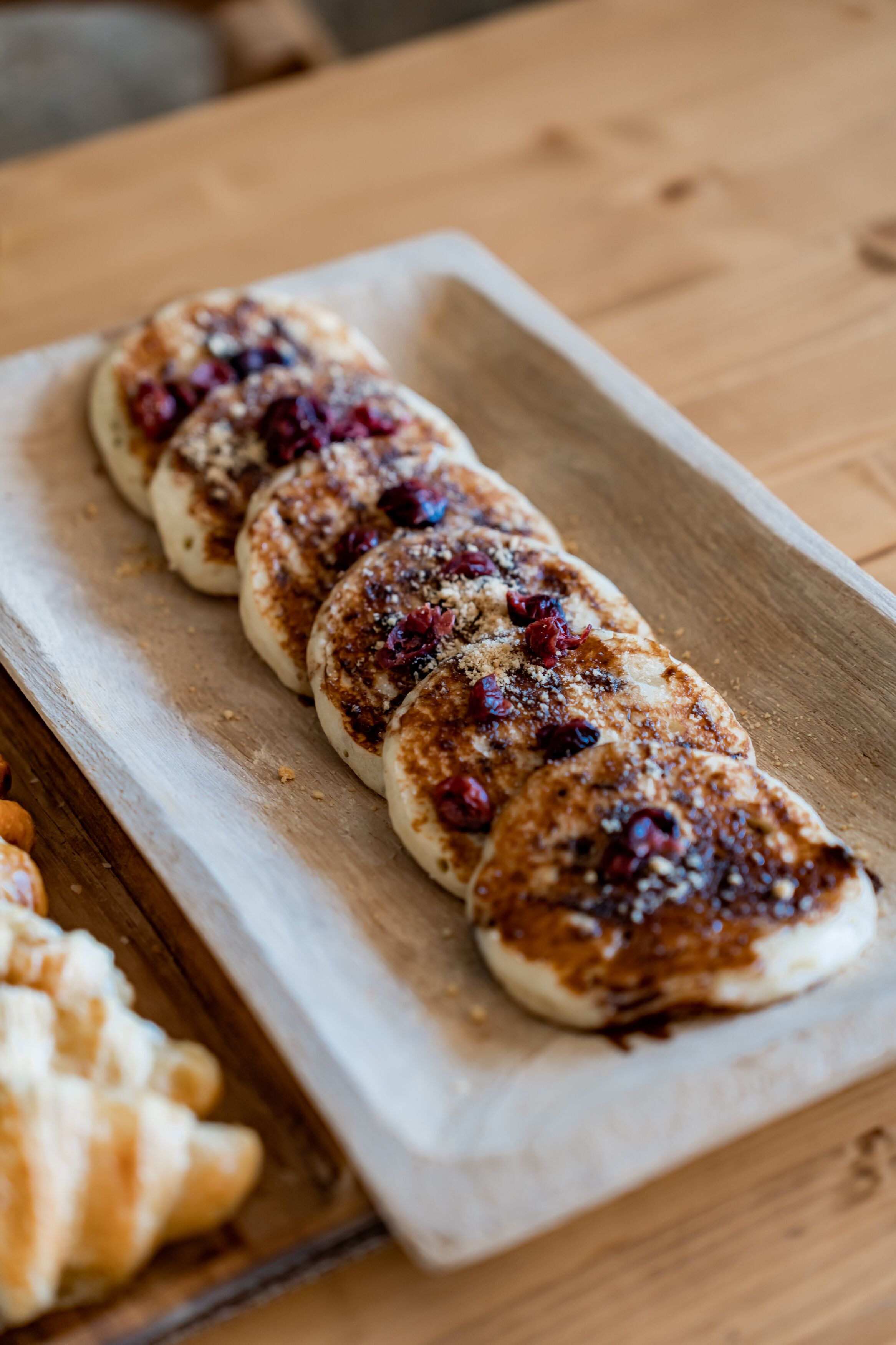 A wooden table with a tray holding several pastries topped with dried cranberries and sprinkled with a brown topping.