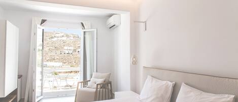 Un dormitorio moderno con una cama grande, una silla y vistas a una colina a través de una puerta abierta.