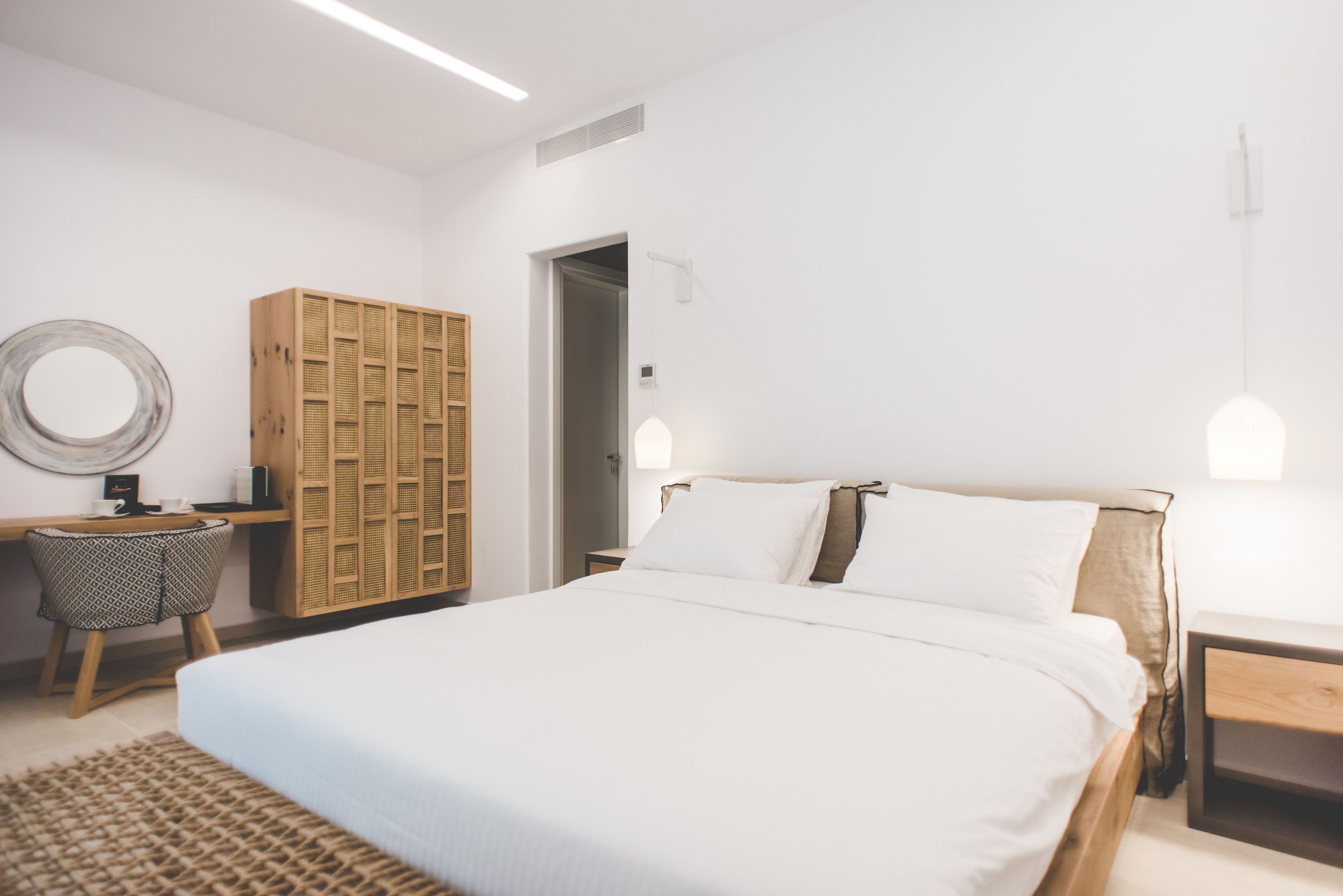 A bedroom with a large bed, a wooden wardrobe, a round mirror, a small table, and a nightstand.