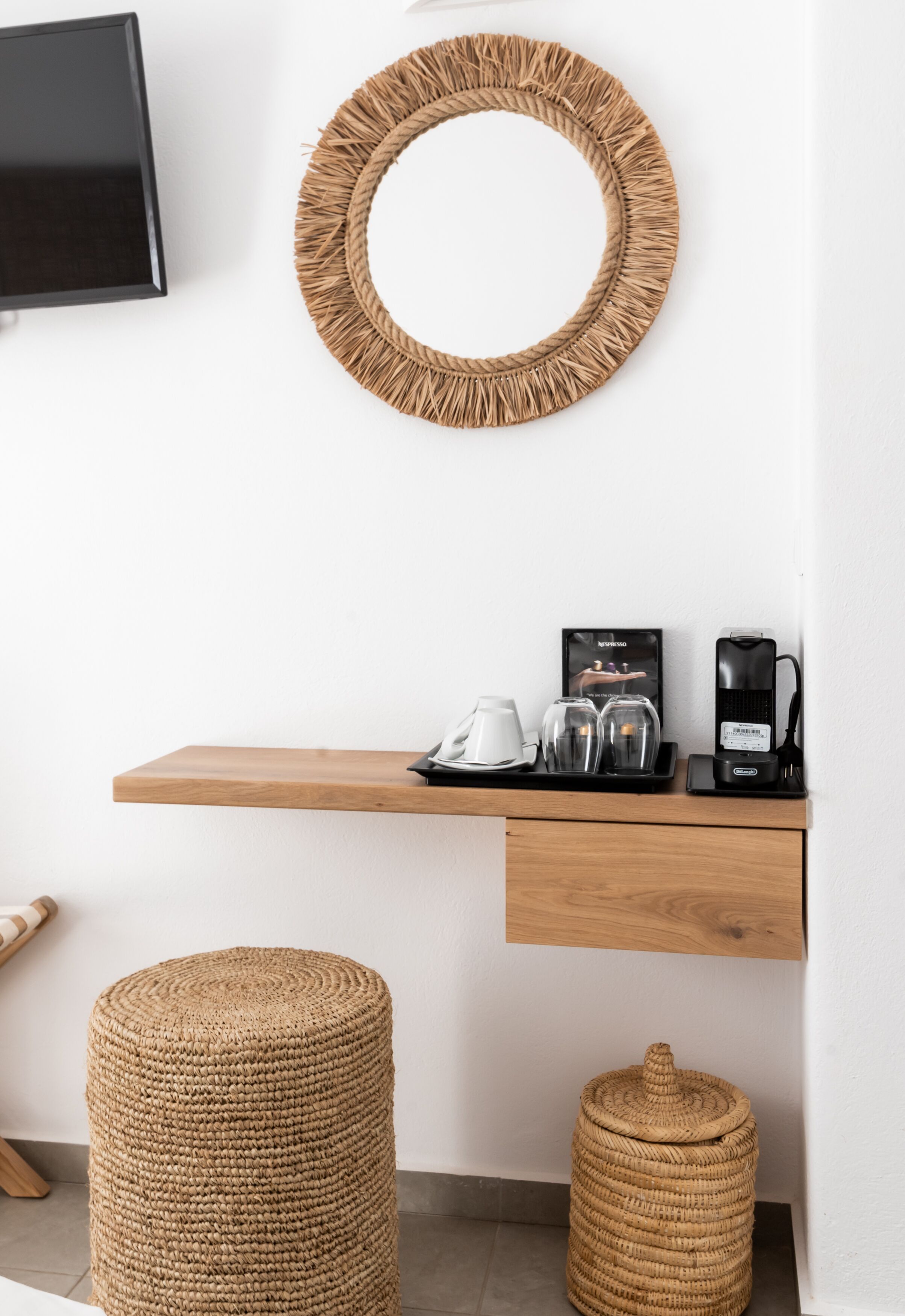 A modern, minimalist room with a wooden shelf holding a coffee maker, glasses, and a cup. A woven basket and stool are on the floor.