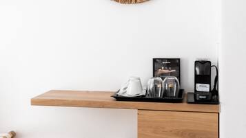 A modern, minimalist room with a wooden shelf holding a coffee maker, glasses, and a cup. A woven basket and stool are on the floor.