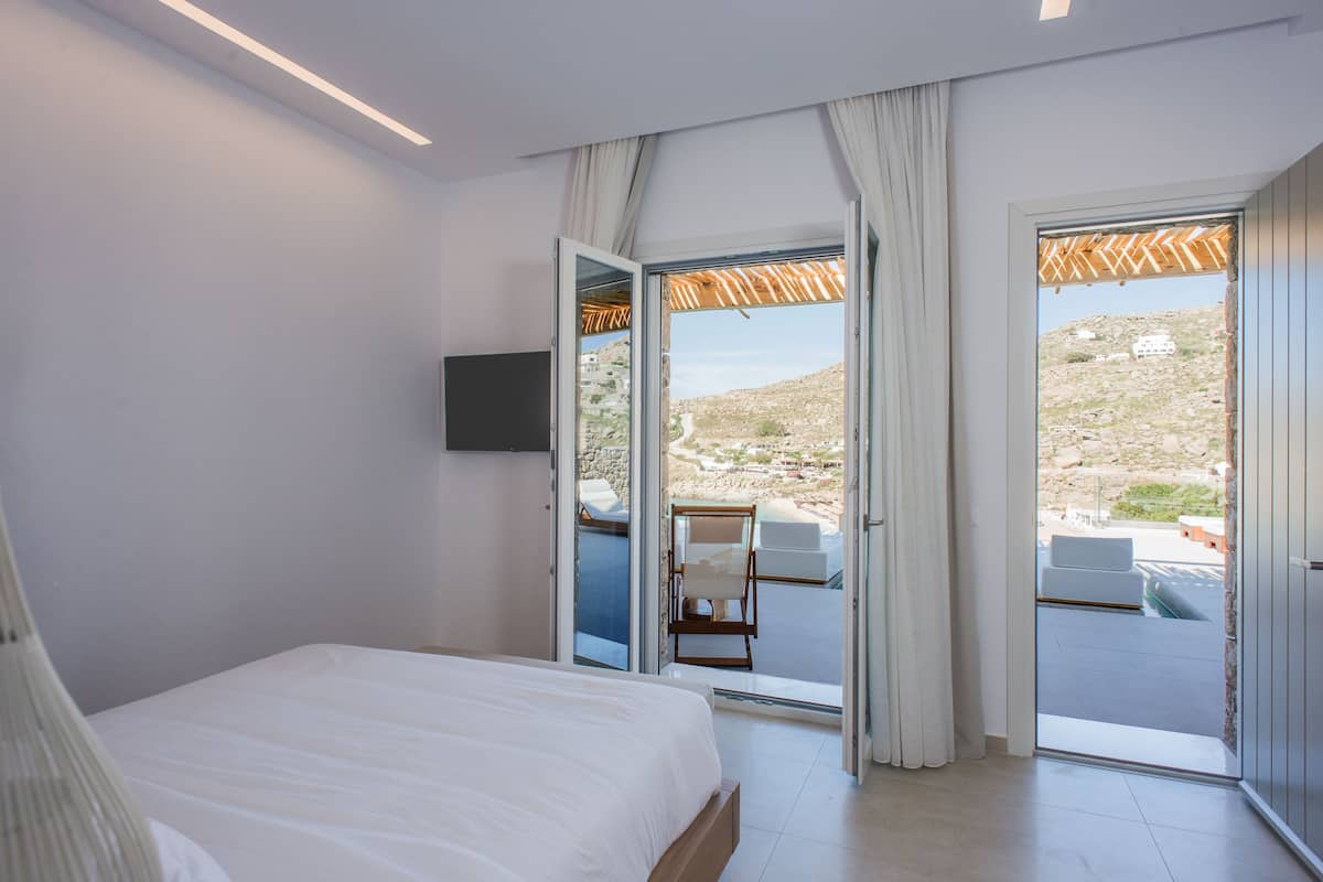 Un dormitorio con cama, televisor y puerta corrediza de vidrio que da a un espacio de estar al aire libre.