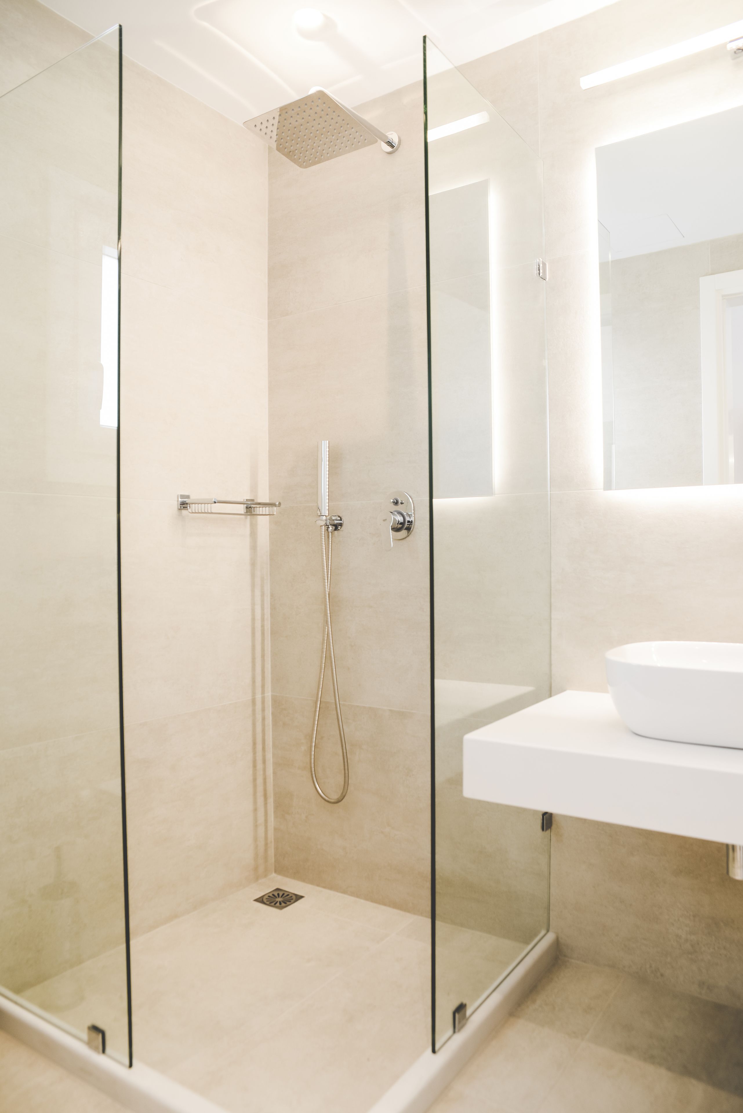 Un baño moderno con ducha de vidrio, un lavamanos blanco y un espejo sobre el lavamanos.
