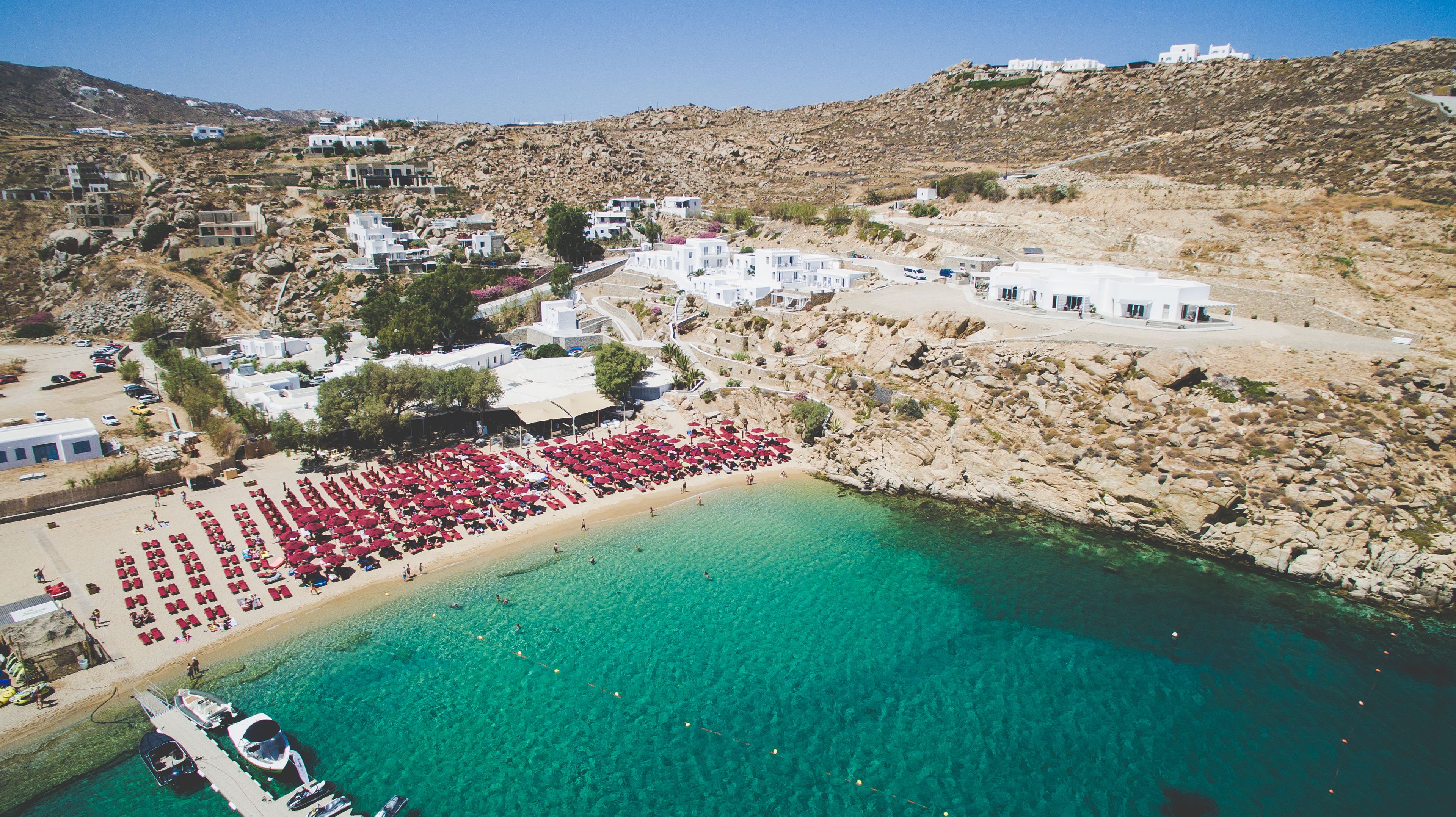An aerial view of a coastal resort with a beach, clear turquoise waters, and white buildings.