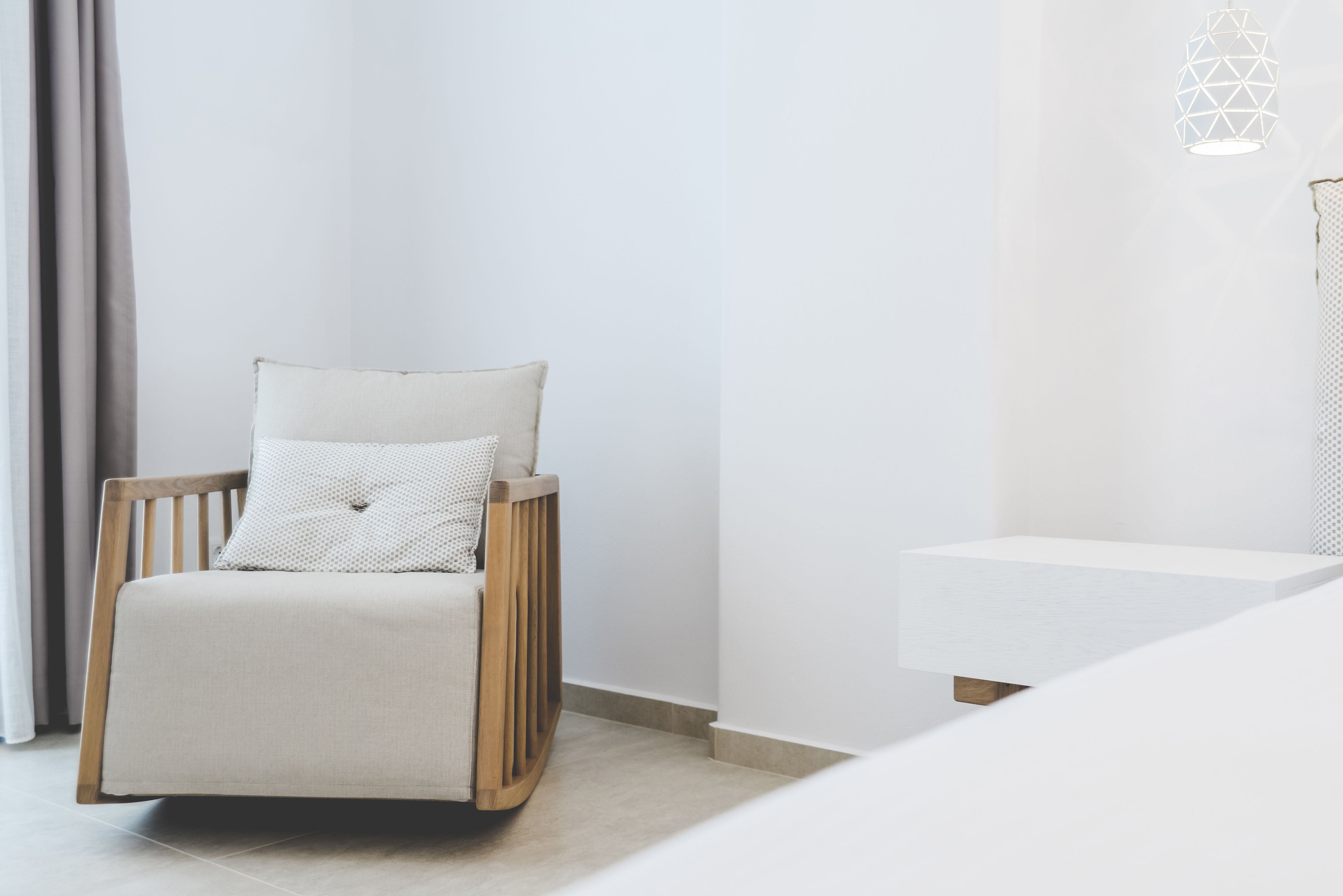 Une pièce au décor minimaliste, avec une chaise en bois, une table de chevet blanche et une suspension au design géométrique.